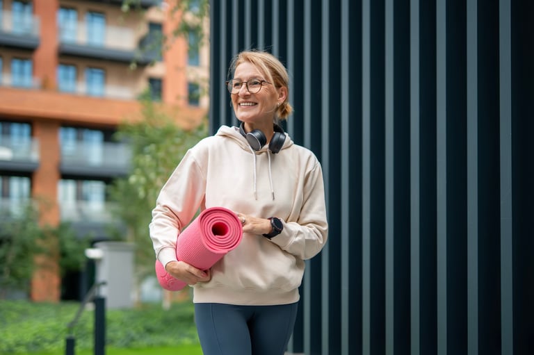 Mature woman smiling and walking through the city with a yoga mat, embodying a healthy active lifestyle and vitality
