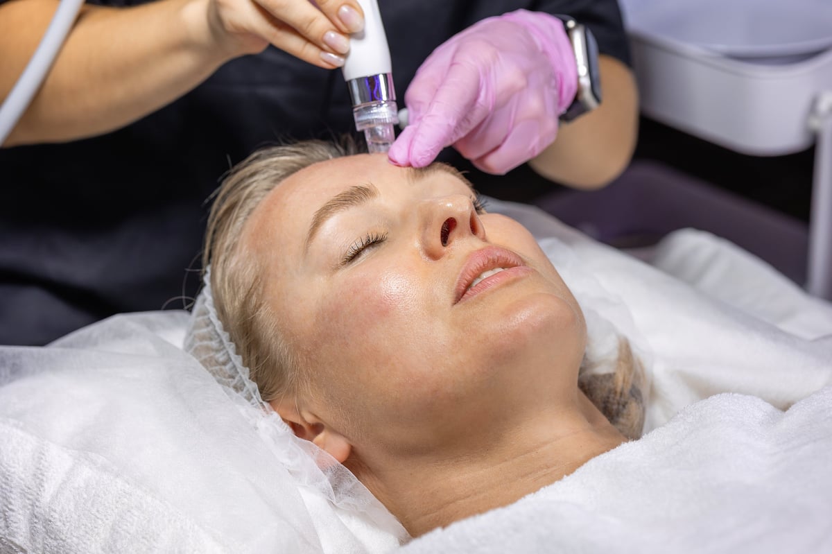 Cosmetologist performs a Hydradermabrasian treatment on a woman's forehead using a hydradermabrasion device to cleanse, exfoliate and hydrate skin during a facial procedure.